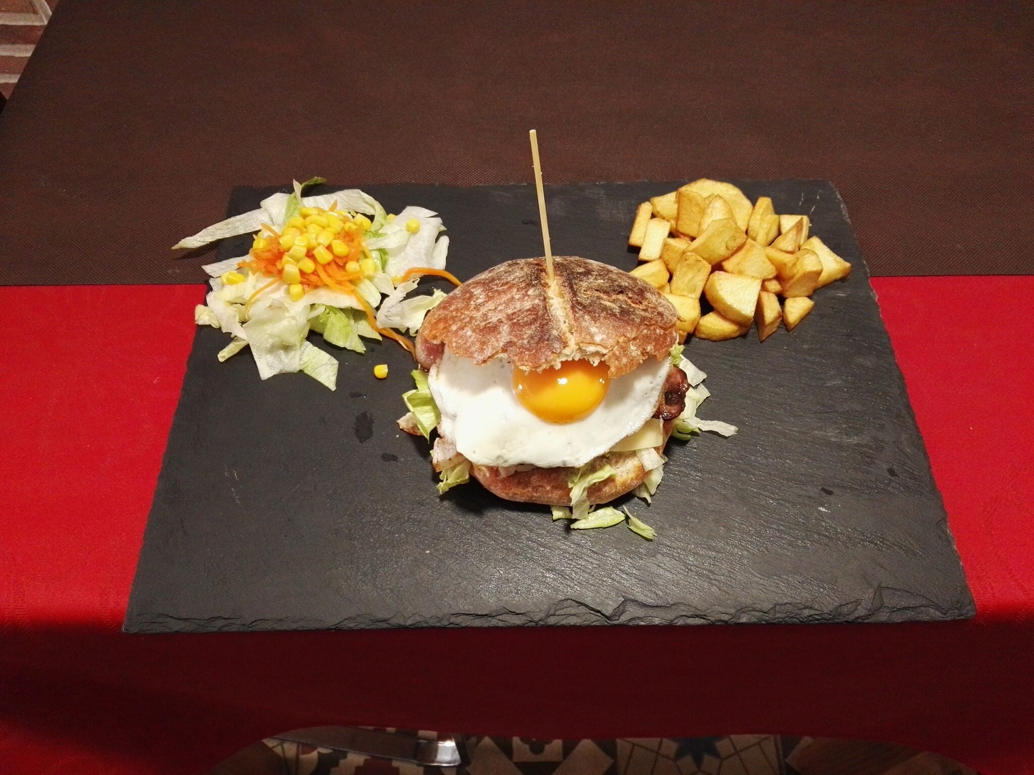 Hamburguesa sobre tabla de pizarra con guarnición